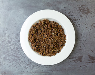 Overhead view of a serving of sweet chocolate granola in a white bowl on a gray tabletop.