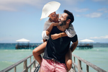 Couple, piggyback and beach deck on a tropical island with love and laughing on holiday. Summer vacation, travel smile and Maldives walk in nature with freedom and happiness by the ocean and sea