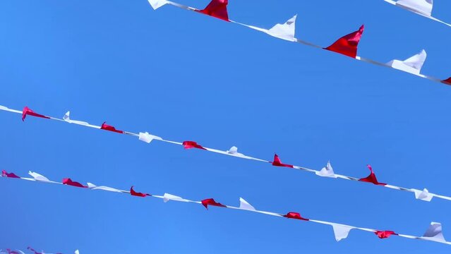festive red and white triangular flags moving in the wind against a blue sky.
