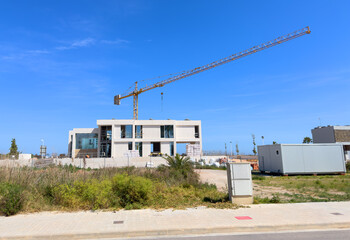 Villa under construction. Tower crane on construction site. Luxury villa construction near beach Mediterranean sea. Construction of modern house on coastline, Spain, Almarda. Home renovation at ocean.