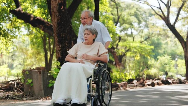 Happy Asian senior man pushing a wheelchair for wife outside in the park, Senior couple and retirement life concept