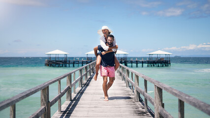 Ocean, dock and a couple playing on vacation for a piggy back, freedom and to relax outdoor with...
