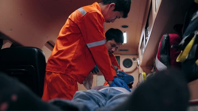 Asian emergency medical technician (EMT) or paramedic making cardiopulmonary resuscitation (CPR) to an unconscious young man after heart attack in ambulance car