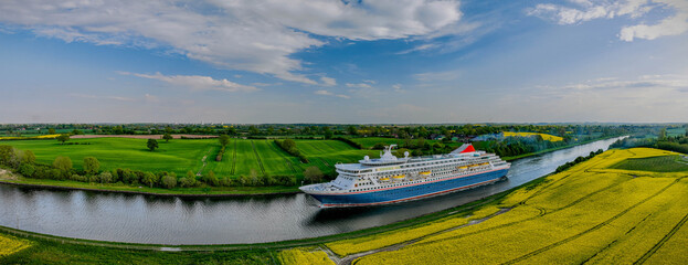 Panoramic view of the Kiel Canal with a cruise ship passing through, surrounded by rapeseed fields....
