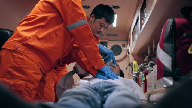 Asian emergency medical technician (EMT) or paramedic making cardiopulmonary resuscitation (CPR) to an unconscious young man after heart attack in ambulance car