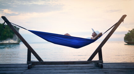 Sunset, hammock and woman on vacation, relax and view on weekend break, getaway and peace. Female person, girl and tourist on summer holiday, water and peace with traveler lying down and tourism