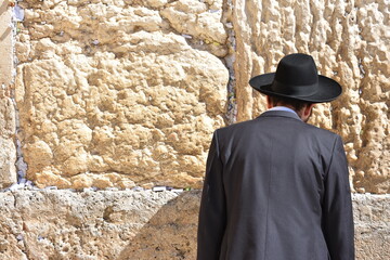 Man standing in a suit and a hat looking at a rock wall in the sun