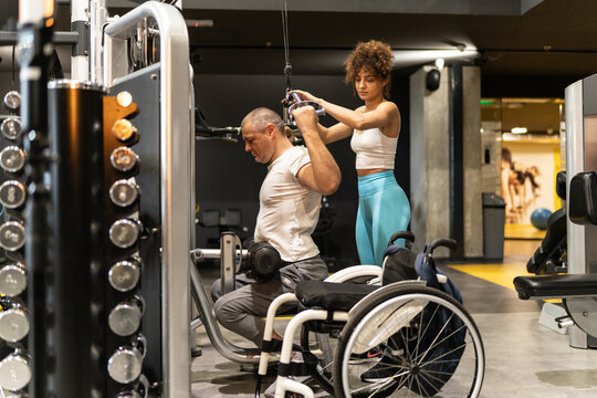 In a display of strength and inclusivity, a person in a wheelchair engages in a workout session with the help of a supportive female fitness instructor.	
