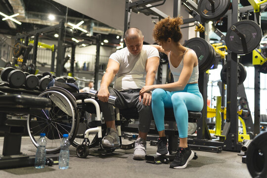 A physically challenged person without obstacles workout at the gym with his female fitness instructor. They're taking a break to refresh and eat energy bars.