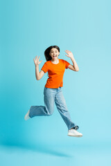 Fototapeta na wymiar Beautiful overjoyed teenage girl wearing stylish jeans, orange t shirt jumping high isolated on blue isolated background 