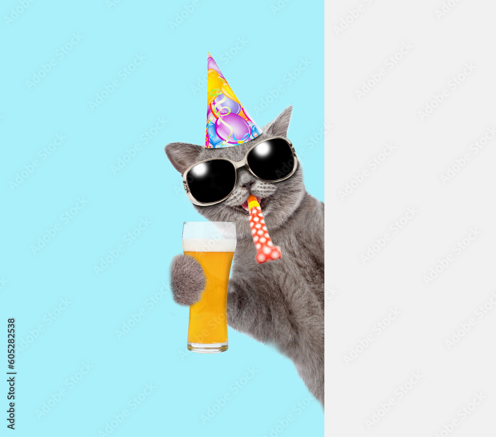 Poster happy cat wearing party cap blows in party hornand looks from behind empty white banner and holds gl