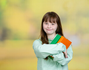 Happy teen girl with Downs syndrom holds a book at summer park