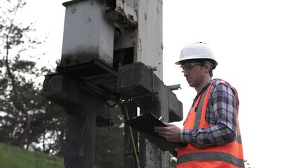An electrical engineer inspects a transformer box and makes entries in a log. Сritical infrastructure.