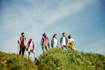 Group of friends walking in meadow on warm, sunny, summer day. Young people standing on hill and...