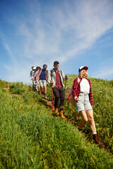 Group of friends, young people walking down the hill path, going hiking in meadow, field, hills on...