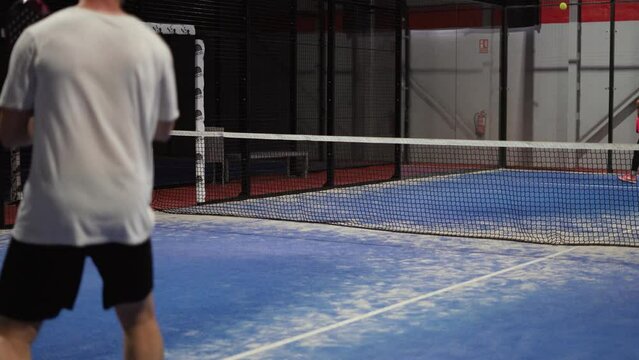 Couple play padel tennis in slow motion. Hitting padel ball in slowmo at indoor padel court.
