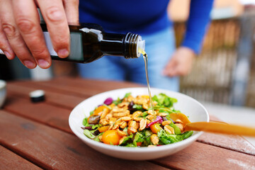 Close up of chef adds oil to vegetables salat with nuts