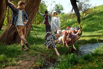 Group of young people, friends walking in forest, going hiking, resting near river on warm sunny day. Relaxation. Concept of active lifestyle, nature, sport and hobby, friendship, fun