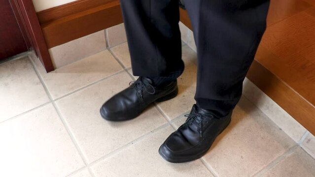 玄関で黒のビジネスシューズを履くスーツ姿の男性