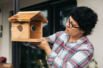Latina woman placing bird house in home garden, DIY concept