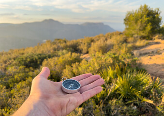 Compass in hand in mountains. Tourist compass for orientation on terrain. Magnetic declination...