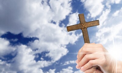 family hands praying hold a Christian cross on sky background.