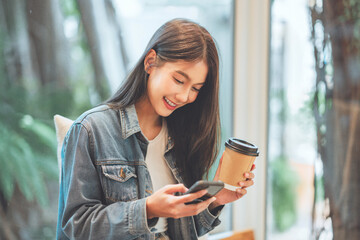 Happy Young Asian beautiful woman using smart phone and drinking coffee in the cafe