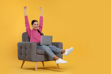 Cheerful woman with laptop sitting in armchair on orange background
