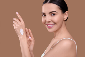 Obraz na płótnie Canvas Beautiful woman with smear of body cream on her hand against light brown background