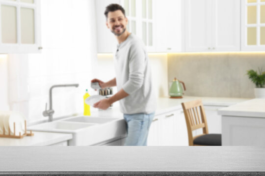 Man doing washing up in kitchen, focus on empty grey stone table