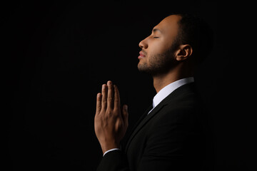 African American man with clasped hands praying to God on black background. Space for text