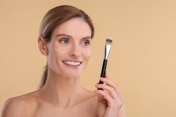 Woman with swatch of foundation holding makeup brush on beige background. Space for text