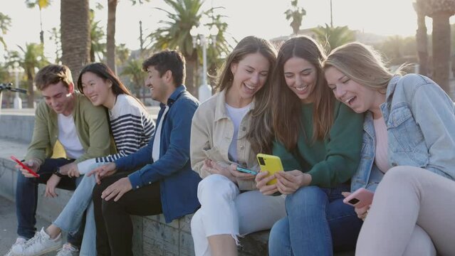 Teenage group of young friends using mobile phones outdoors. Millennials having fun watching social media content on smartphone app. Technology and youth community concept.