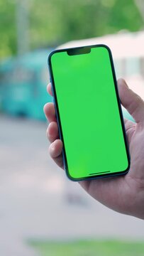 Close Up Male Hand Holding Phone With Green Mock-up Screen On Background of Tram Traffic