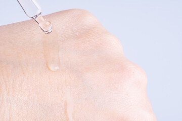 Macro photo of woman's hand and pipette with oil or gel. Transparent drop of essence, oil or gel drops from the pipette on the  extra dry skin