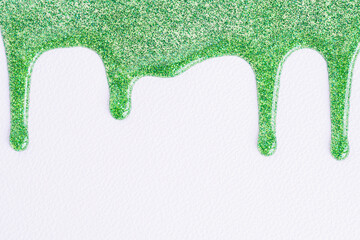 Green glitter sparkle confetti background liquid drops of paint color flow down on white canvas. Macro photo. Green glitter paint dripping on the white wall