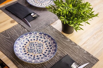 Dinner table with placemats, plates, cutlery and a decorative plant in a street cafe