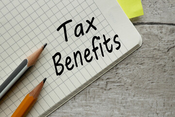 text TAX BENEFITS on the corner of the notebook by hand. wooden background