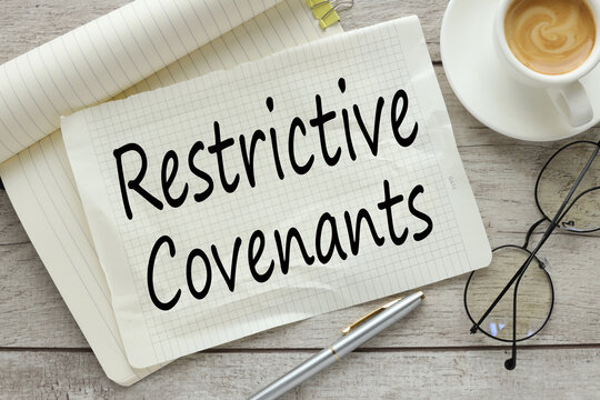 Restrictive Covenants On a wooden background, a notepad with text with a cup of coffee and glasses