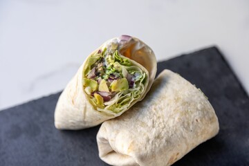 Closeup of vegetable wrap cut into two pieces on a black stone