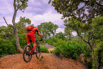 Fototapeta na wymiar Unrecognisable mountain biker rides a beautiful trail on red earth, Massa Marittima, Tuscany, Italy