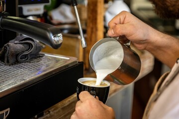 Person pouring milk into a cup of coffee in a cafe