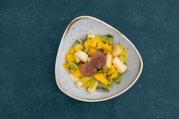 Top view of bright juicy and delicious fruit salad in a plate against green background