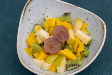 Closeup of bright juicy and delicious fruit salad in a plate against green background