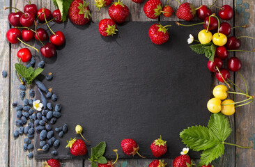 Mix of delicious juicy spring berries on a black stone board