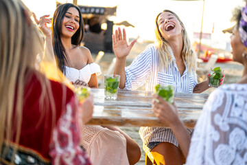 Happy girls having fun drinking cocktails at bar on the beach, young women in holiday smiling and laughing