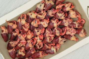Chicken hearts in board on wooden background. Raw meat. Top view.
