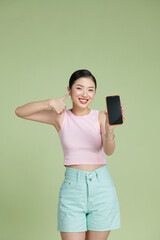 Beautiful woman showing a smart phone with thumb up isolated on a green background