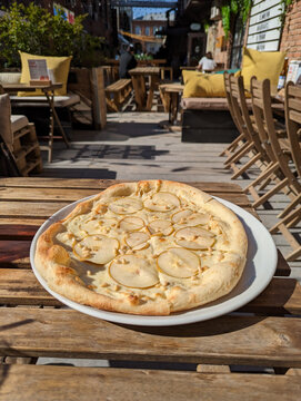 pear and cheese pizza on a white plate in a street cafe stands on a wooden table