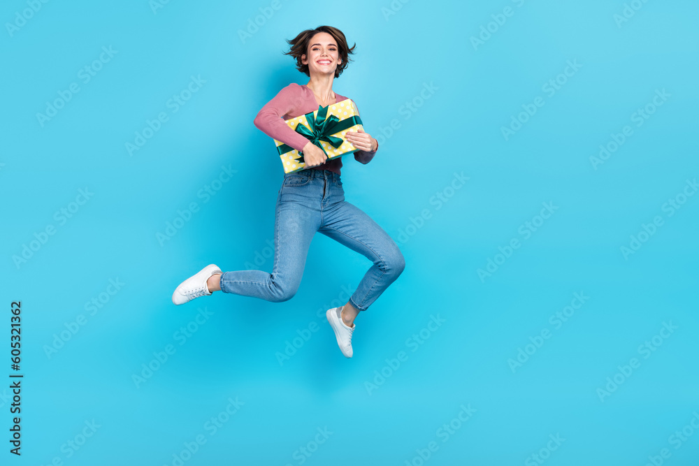 Poster full body photo of carefree energetic lady hands hold giftbox jumping empty space isolated on blue c